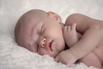 Newborn baby sleeps sweetly on light background. Portrait of month-old baby with tender skin on changing table in room. Close-up of beautiful child on white background. Concept of new life