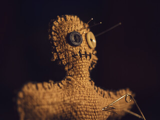 A voodoo doll made of burlap, with buttons for eyes, pierced with many needles right through the heart, close-up. The concept of unrequited love, revenge on a person for cheating or causing pain