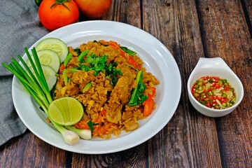 Authentic Thai old style fried rice in dark soy sauce served with spring onion, cucumber slices and lime having chilli in fish sauce as side dish on wooden table.
