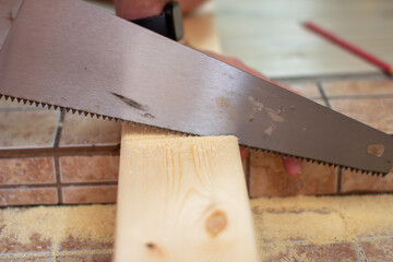 closeup of a young man sawing a wooden board with a handsaw