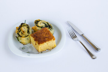 A slice of sweet cake and spinach pie in a plate on black surface with cutlery set.