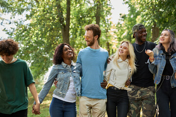 happy diverse african and caucasian people walk together in the park, have conversation and laugh. tolerance, international friendship concept