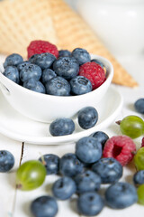 Blueberries and raspberries in a white bowl and on a white wooden table.