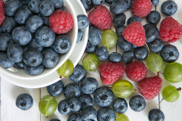 Blueberries, raspberries and gooseberries on a white table. Top view close up.