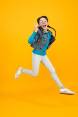 Fototapeta na wymiar Full length portrait of happy little schoolgirl jumping on yellow background. teen girl on school break. childhood happiness. finally graduated. movement and people concept. crazy kid jumping in air