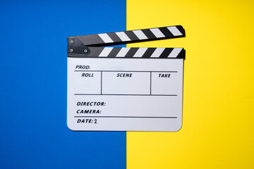 movie clapper on blue and yellow table background; film, cinema and video photography concept