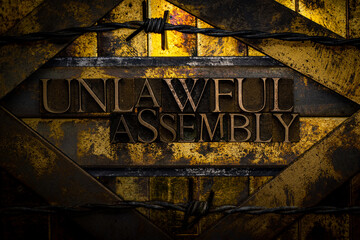 Unlawful Assembly text formed with real authentic typeset letters on vintage textured silver grunge copper and gold background
