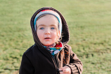 Toddler girl on grassy field opening zipper of cardigan