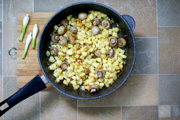 fried potatoes with mushrooms and grinnery in a pan on a wooden cutting board top view      
