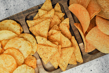 Chips, snacks and crackers on a wooden board. Fast food.