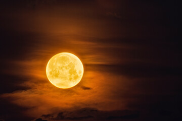 Bright yellow moon in dark sky and illuminates the clouds
