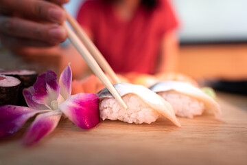 Eating sushi Japanese food - Action of woman is using chopsticks to picking up a piece of sushi from wooden plate. Close-up and selective focus photo.