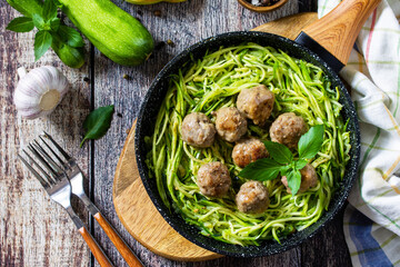 Healthy food. Cooked zucchini noodles with meatballs in a cast iron skillet on a rustic table. Top view flat lay background. - obrazy, fototapety, plakaty