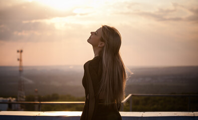 young blonde woman enjoys life in the rays of the sunset