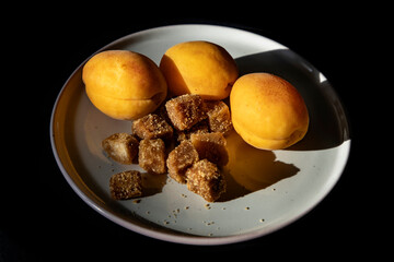 Apricots and brown sugar cubes on a white plate on a black background