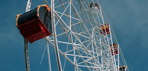 Ferris wheel with colored red and orange cabs in the sky. Sunny clear sky in the amusement park.