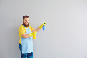 Cleaning service and housework concept. Happy funny guy with detergents on grey background, space for text