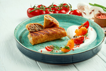 Classic Ukrainian pancakes (crepes) stuffed with meat on a blue plate with sour cream on a white...