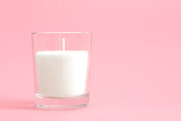 White wax candle in glass Isolated on pastel pink background, mock up