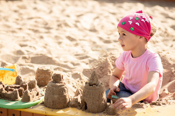 Small cute girl shares a sand castle in a sandbox