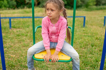 Little girl crying sitting on a swing at the playground