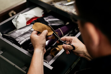 Obraz premium Male cobler sitting at his vintage looking shop and cutting leather fabric for shoe repairing