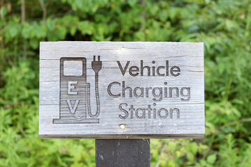 Wooden sign for electric vehicle charging with trees in the background.