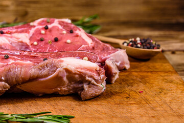 Raw ribeye steak, wooden spoon with spices and rosemary on a cutting board
