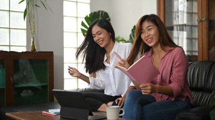 Asian women are sitting and relaxing together on the black leather sofa.