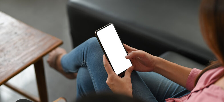 Cropped image of a beautiful woman is using a mockup smartphone while sitting on a black sofa.