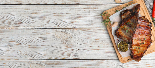 Serving board with tasty grilled ribs and space for text on white wooden table, top view. Banner...