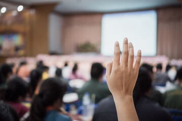Obraz premium Audience raising hand while speaker on stage at conference to answer question while speaker speech at seminar hall with crowd groups in business and education concept
