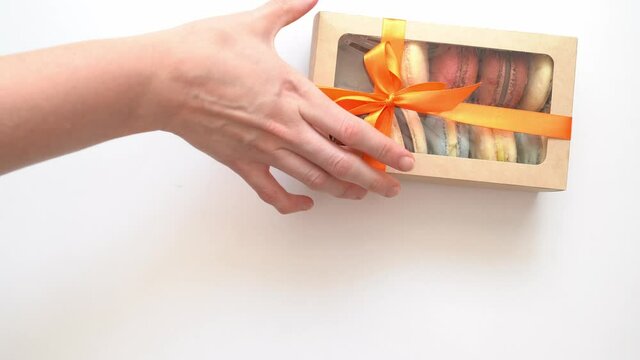 pack with ribbon and inside macarons enters frame on white table. several times