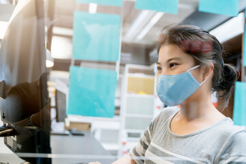 Fototapeta na wymiar attractive asian female navy blue sweater working while wearing protective virus mask working in co woking space that have plastic partition social distancing for seat new normal lifestyle