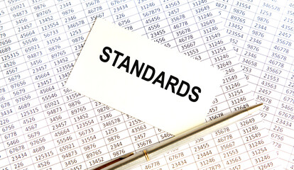 Obraz premium On the table is an accounting report, on it is a white card with the inscription STANDARDS, next to the pen.