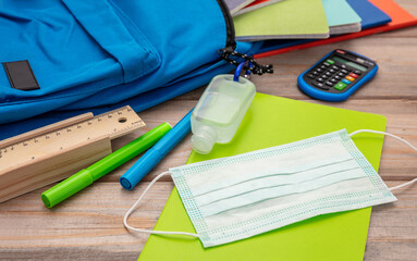 Sanitizer gel, medical mask and school supplies on a student desk