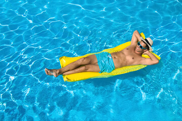 Young man with inflatable mattress in swimming pool. Summer vacation
