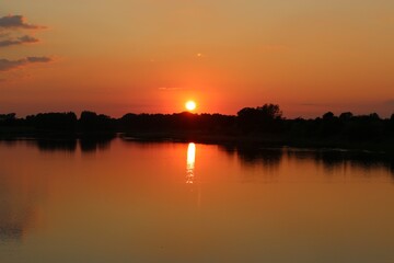 A sunset at a lake with trees on the bank of the lake