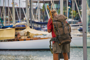 Fototapeta premium Refugee man with his backpack loaded, looking for food in the garbage in the richest neighborhood in the city. social injustice