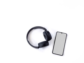 Black wireless headphone and mobile smartphone with a blank screen mockup lay on the surface of a white background