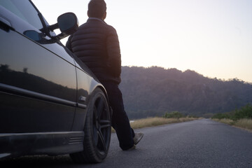 Rear view of the man sitting in front of the car and enjoying sunset
