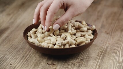 Woman Picks Up A handful Cashew, To Eat, From Her Bowl. took a nut on the right side