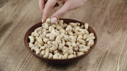 Woman Picks Up A Single Cashew, To Eat, From Her Bowl. took a nut on the right side