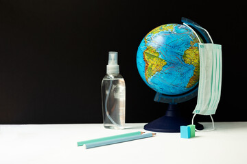 Globe, sanitizer and medical mask on a background of black chalk Board. the concept is back to school, in a new reality.