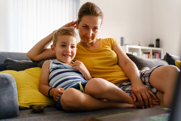 Fototapeta na wymiar Small caucasian boy little child sitting on bed by mature woman - Mother and son at home watching content on laptop computer making video call having fun smiling - childhood leisure activity concept