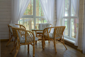 Rattan furniture on the summer porch. Outside the window is a pine forest.