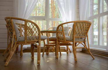 Rattan furniture on the summer porch. Outside the window is a pine forest.