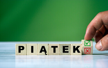 The hand turns the wooden cube and changes the polish word PIĄTEK (english friday)  with green...