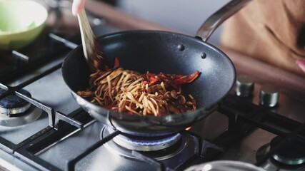 Cook frying noodles and vegetables in wok pan