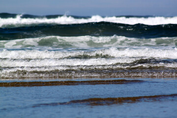 Beach scene with blue and white surf, crashing waves, and smooth sand dunes
